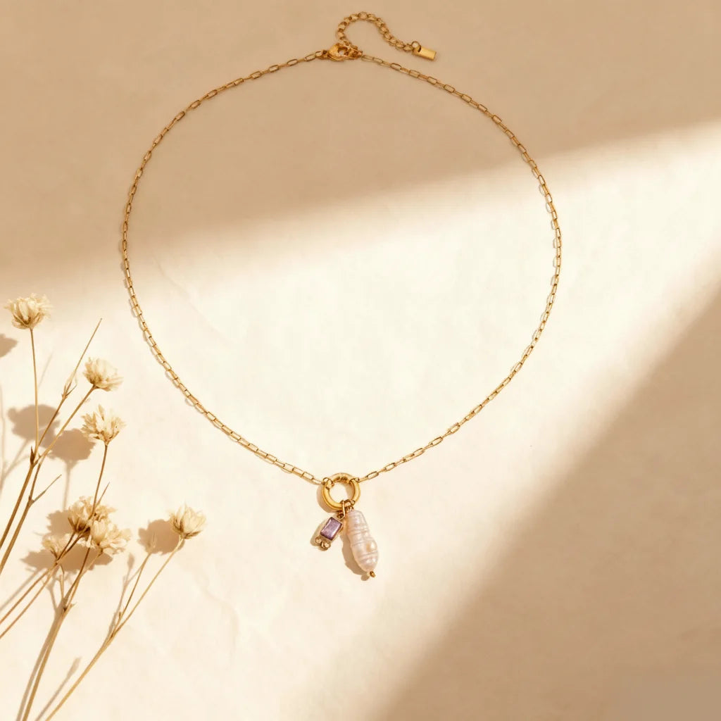 A full display of The Astoria Necklace for February, showcasing the royal amethyst purple birthstone charm next to its unique pearl.