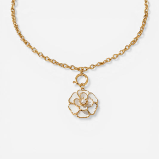 A detailed studio shot of The Fleur Pendant by Luminova, showcasing the white enamel camellia flower on a gold rolo chain, styled in warm sunlight.