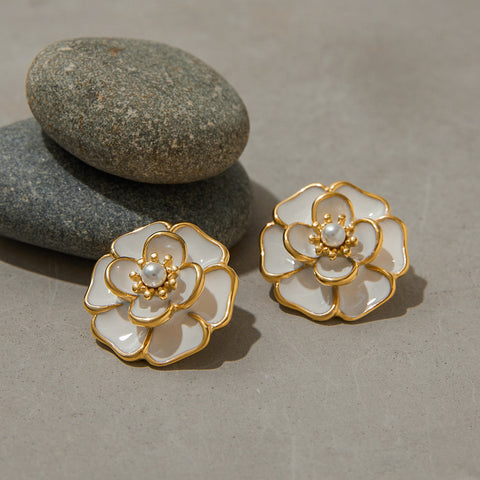 The Fleur camellia earrings resting on smooth grey stones, highlighting the beautiful contrast between the organic and the refined.