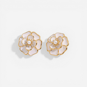 A detailed studio shot of The Fleur Studs by Luminova, showcasing the iconic white enamel camellia flower design with a central pearl and gold trim.