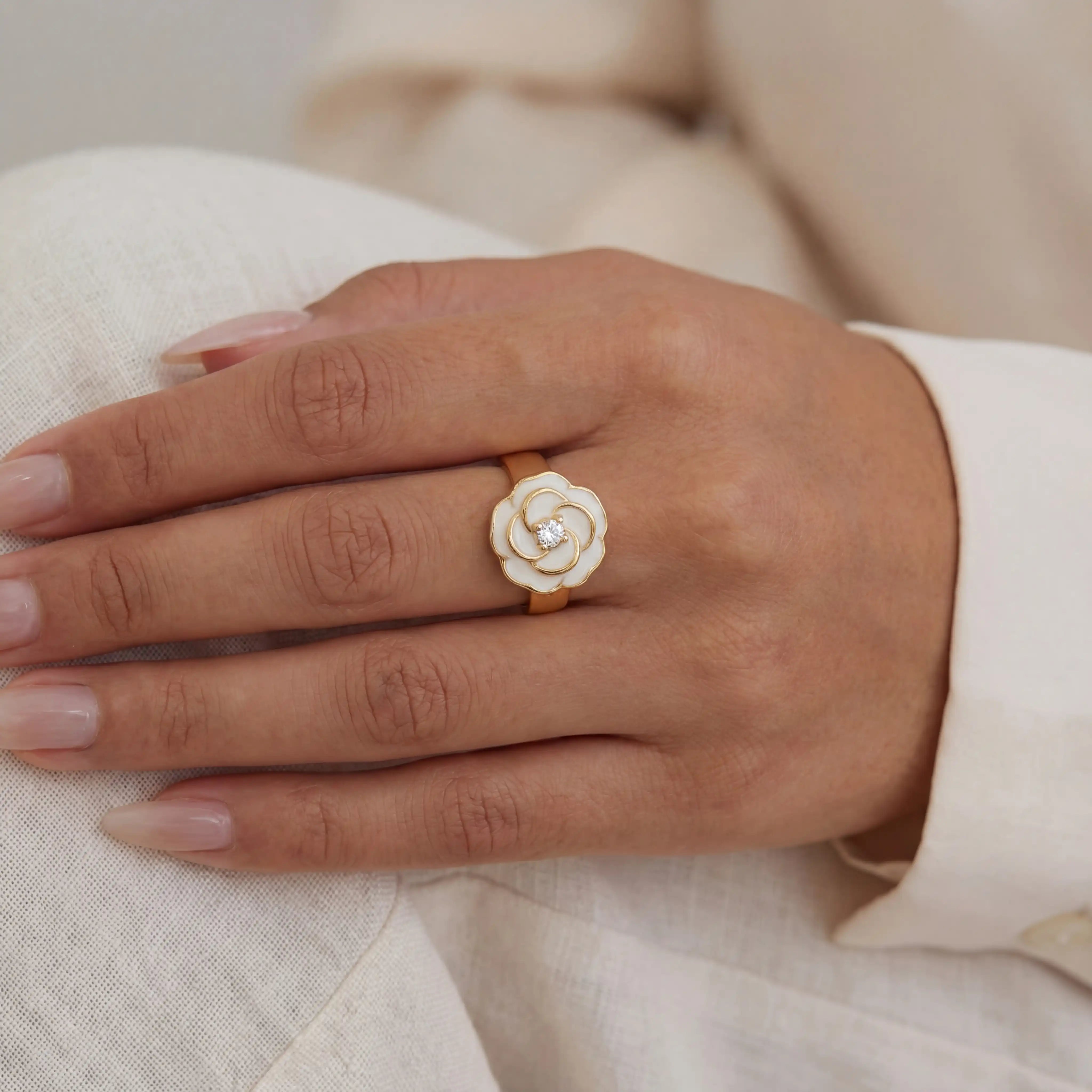Close up of woman wearing white enamel camellia ring with gold details romantic jewelry style. Main image
