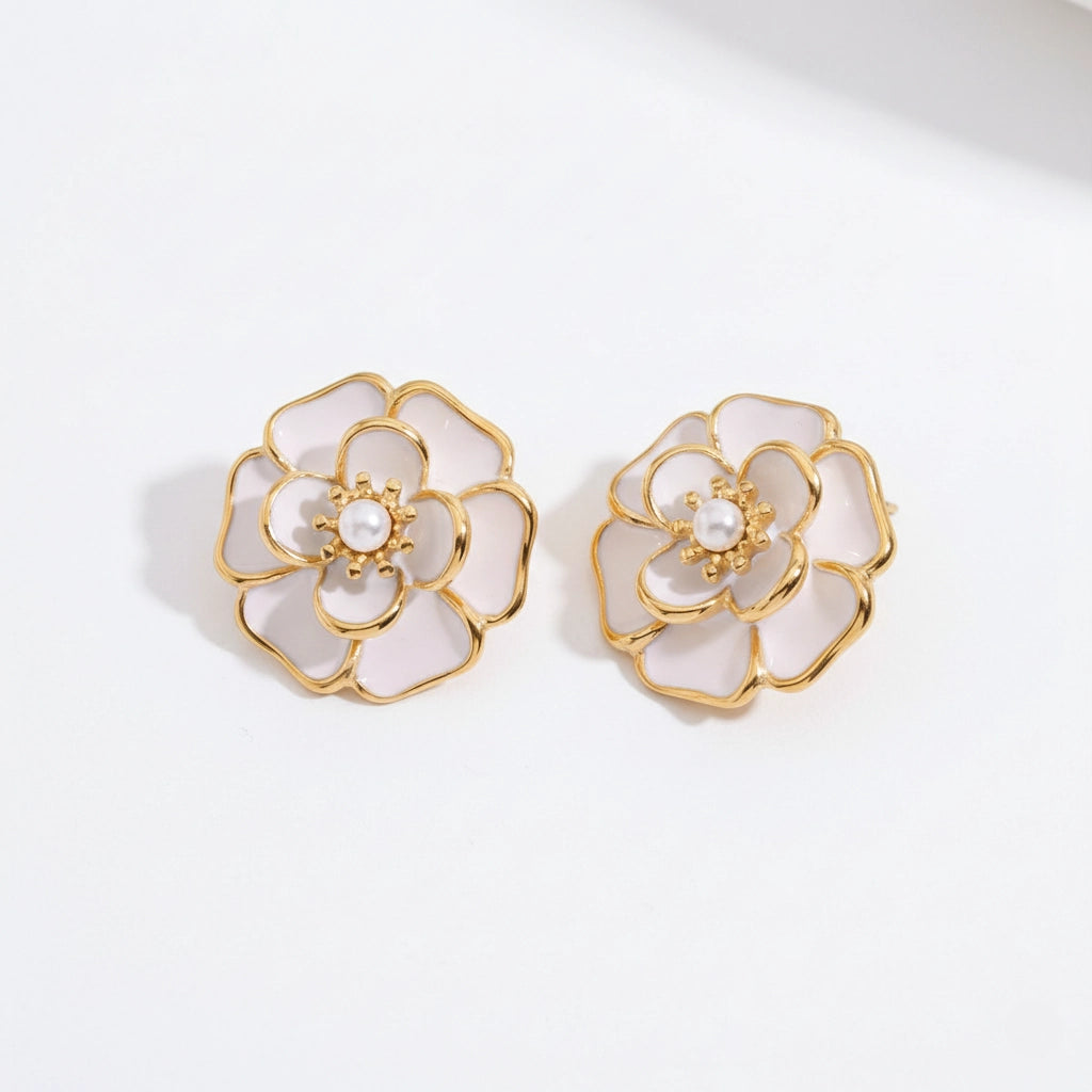 A detailed studio shot of The Fleur Studs by Luminova, showcasing the iconic white enamel camellia flower design with a central pearl and gold trim.