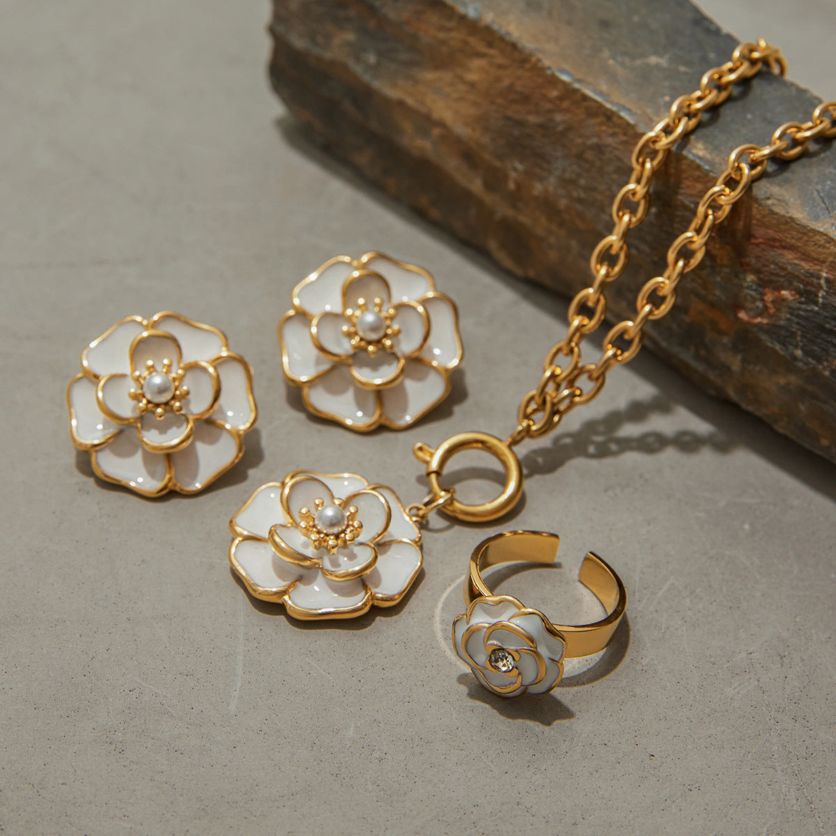 The entire Fleur jewelry set, including the camellia necklace, studs, and ring, styled elegantly on natural stones to highlight their quality.