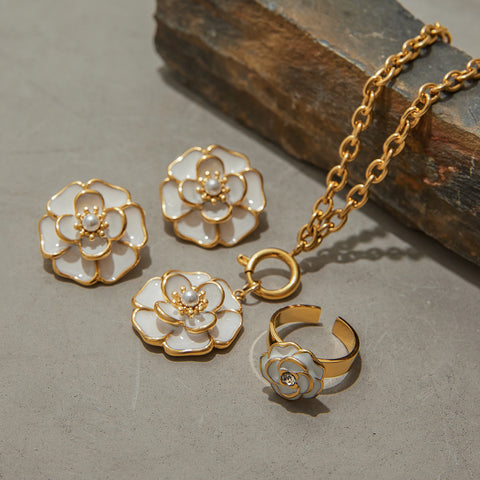 The entire Fleur jewelry set, including the camellia necklace, studs, and ring, styled elegantly on natural stones to highlight their quality.