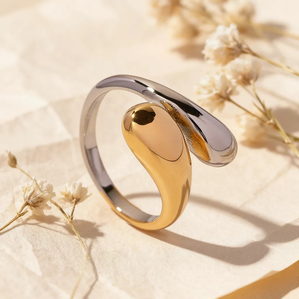 A detailed product shot of the two-tone Fluid Pebble Ring by Luminova, showcasing its sculptural, yin-yang inspired design in gold and silver, styled with dried flowers. Main image