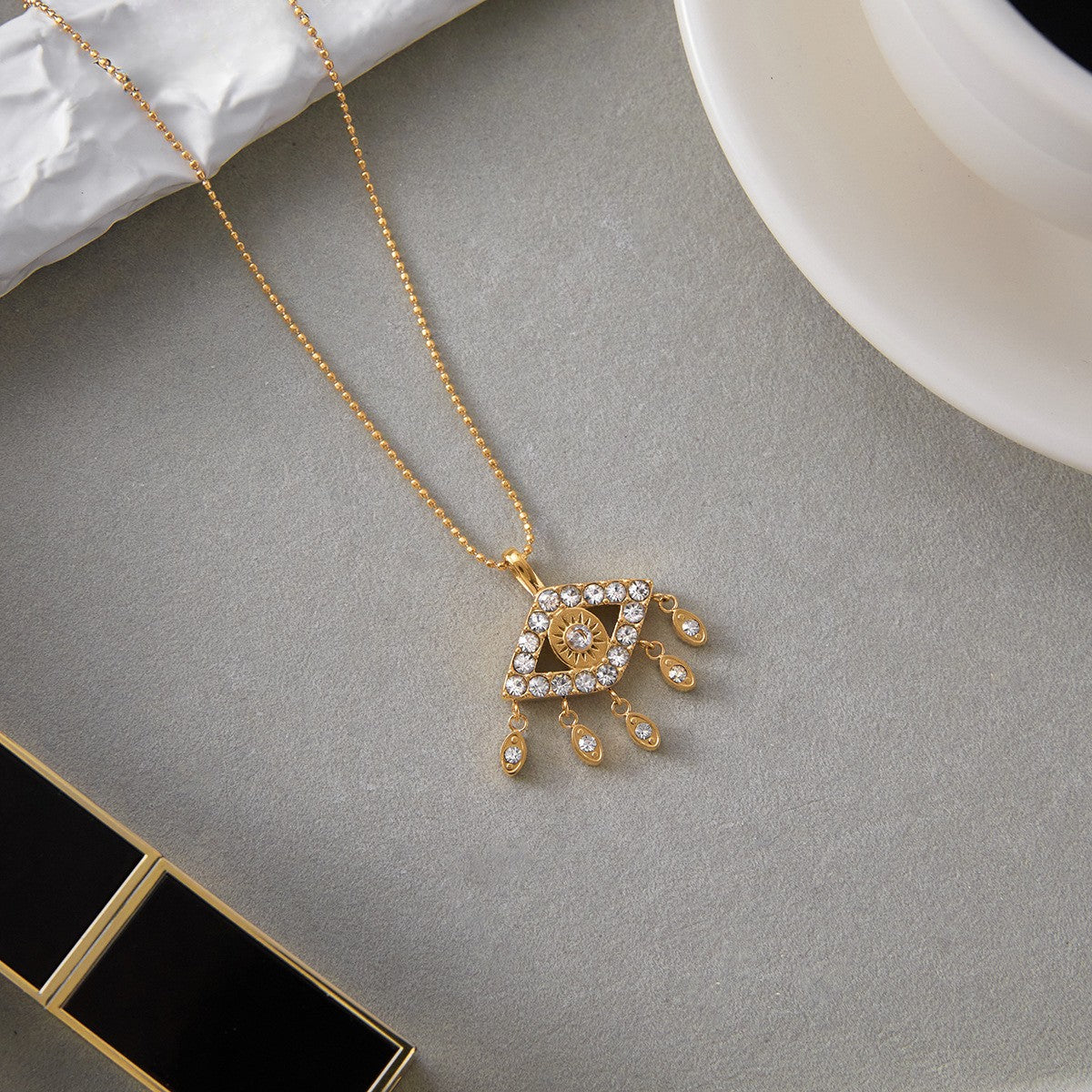 The Fortuna evil eye necklace casting a soft shadow next to a cup of coffee, showing its intricate crystal details and delicate chain.