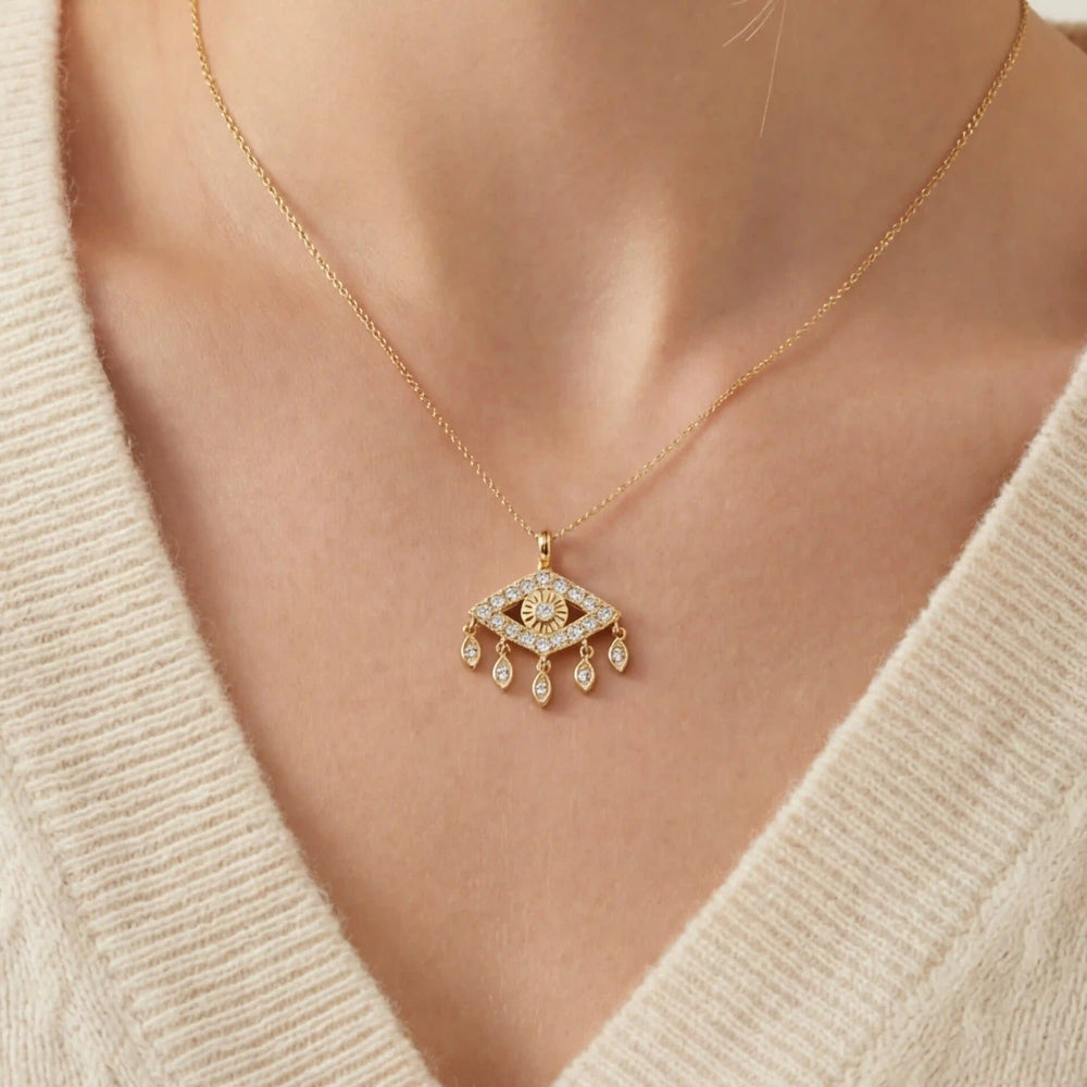 Close up of woman wearing gold Fortuna necklace with sparkling evil eye pendant and dangling charms.