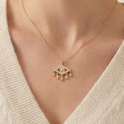 Close up of woman wearing gold Fortuna necklace with sparkling evil eye pendant and dangling charms.