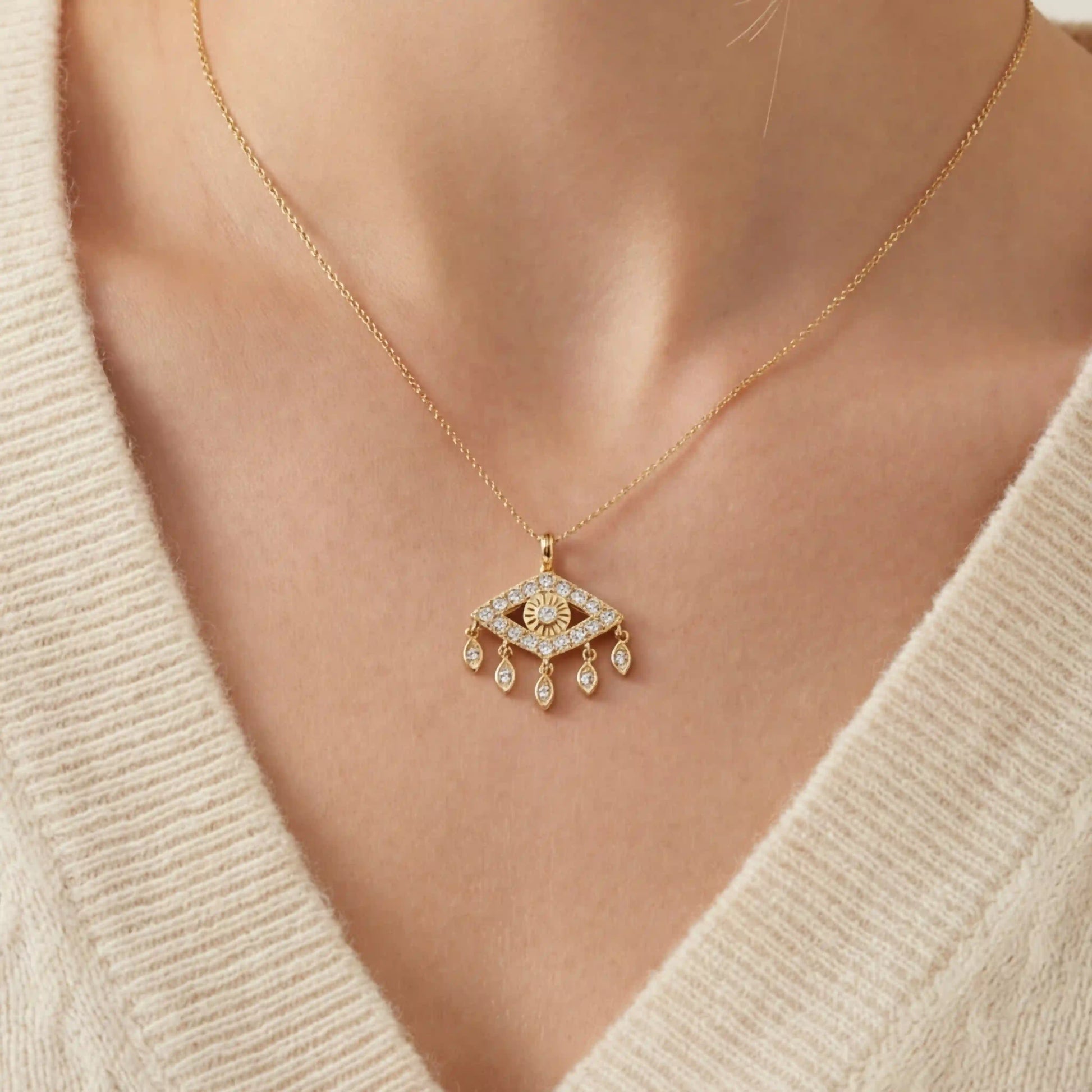 Close up of woman wearing gold Fortuna necklace with sparkling evil eye pendant and dangling charms.