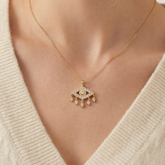 Close up of woman wearing gold Fortuna necklace with sparkling evil eye pendant and dangling charms.