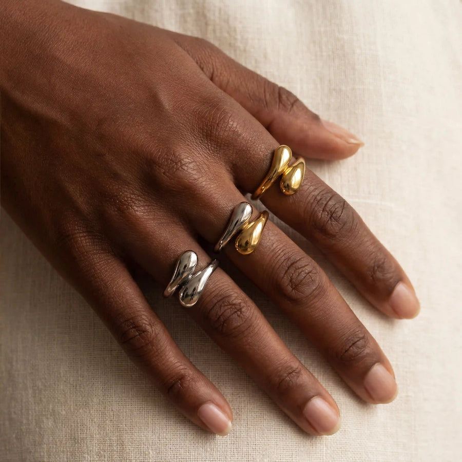 Close up of woman's hand wearing gold silver and mixed metal Gemini open rings with teardrop design.
