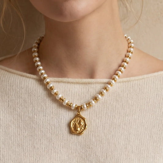 Close up of woman wearing gold beaded pearl necklace with organic coin pendant on collarbone.