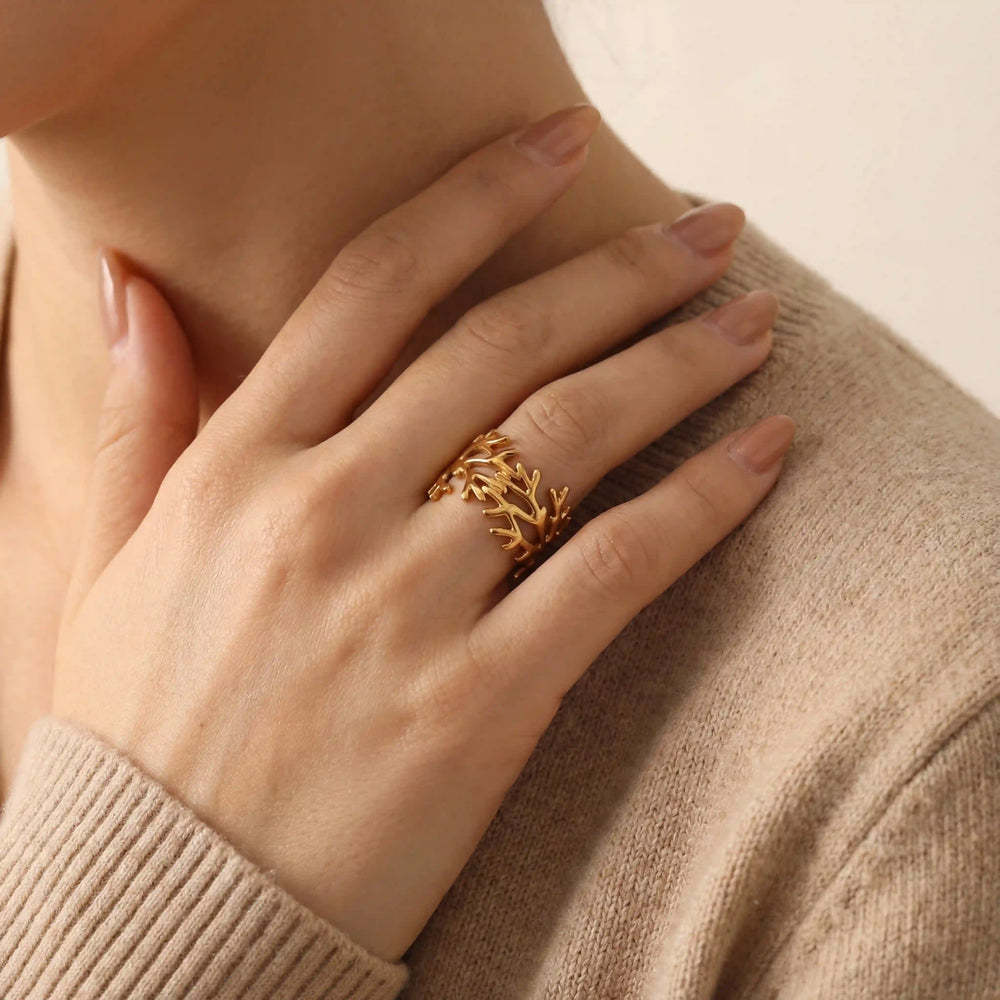 Close up of woman's hand wearing gold coral branch ring on ring finger beige sweater.