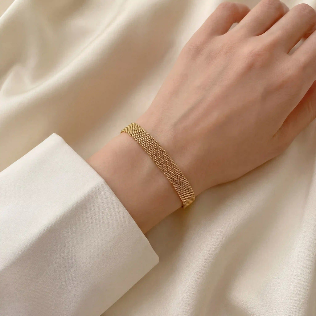 Close up of woman's wrist wearing gold mesh chain bracelet soft woven texture.