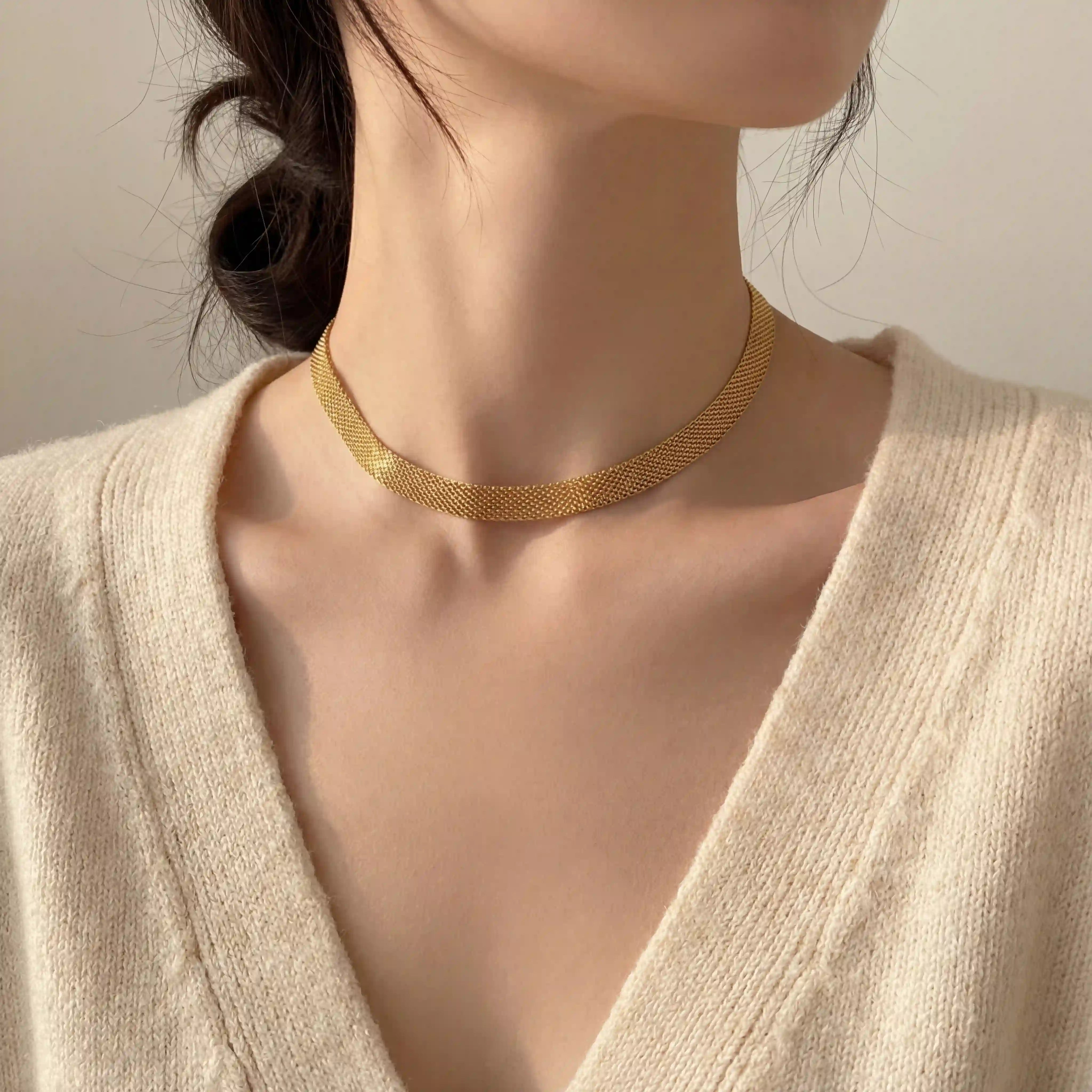 Close up of woman wearing gold mesh chain necklace flat woven choker style with cream cardigan.