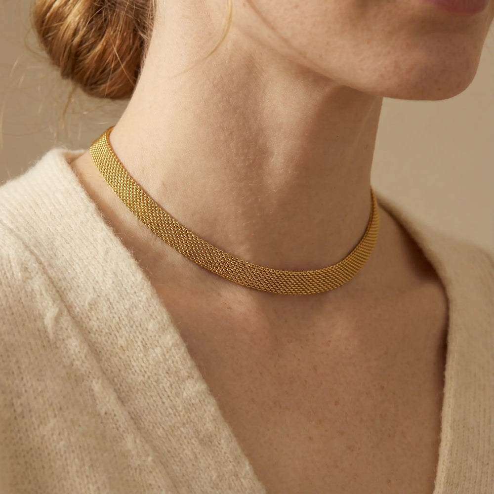 Close up of woman wearing gold mesh chain necklace flat woven choker style with cream cardigan.