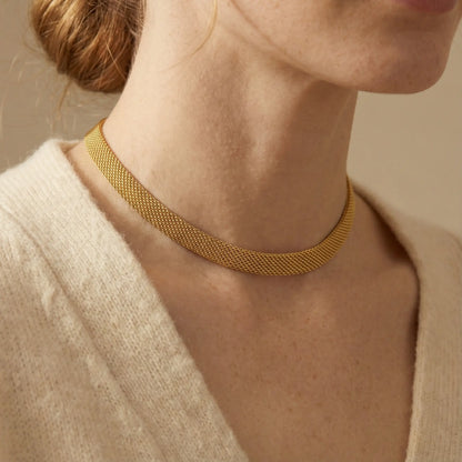 Close up of woman wearing gold mesh chain necklace flat woven choker style with cream cardigan.