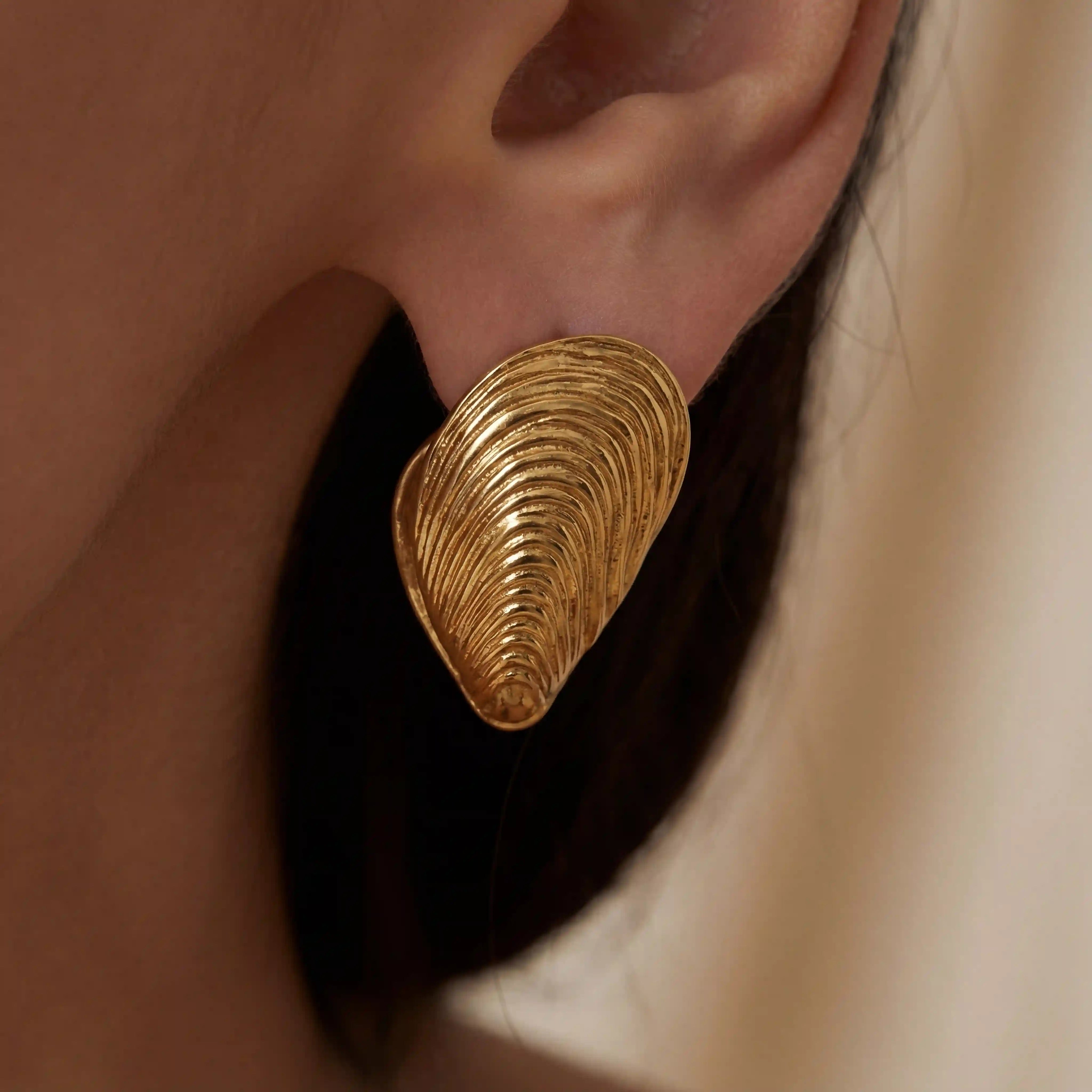 Close up detail of textured gold mussel shell earring on model ear.