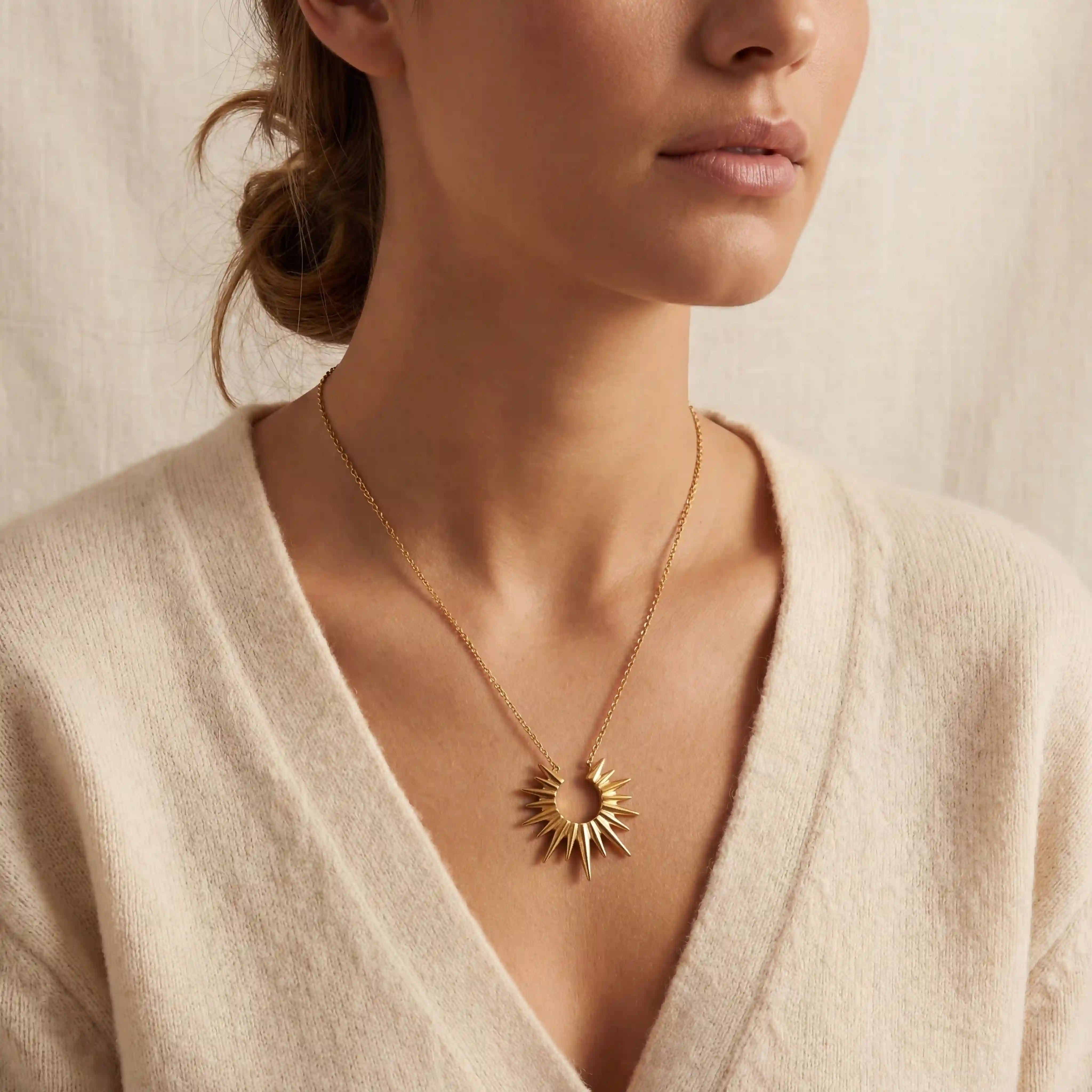 Close up of woman wearing Helios gold sunburst necklace with beige cardigan everyday style.
