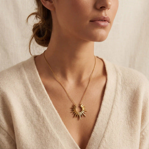 Close up of woman wearing Helios gold sunburst necklace with beige cardigan everyday style.