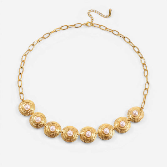 A detailed studio shot of The Hera Necklace by Luminova, showcasing the vintage-style pearl and textured gold medallion collar on a soft, warm background.