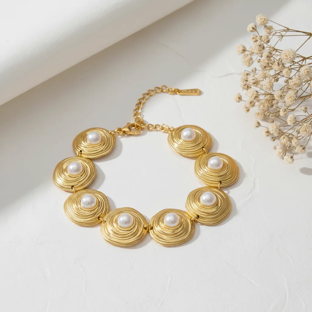 A detailed studio shot of The Hera Bracelet by Luminova, showcasing its vintage design with a series of textured gold medallions, each centered with a lustrous white pearl.