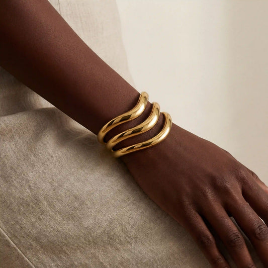 Dark skin model styling sculptural gold instant stack cuff bracelet on wrist.