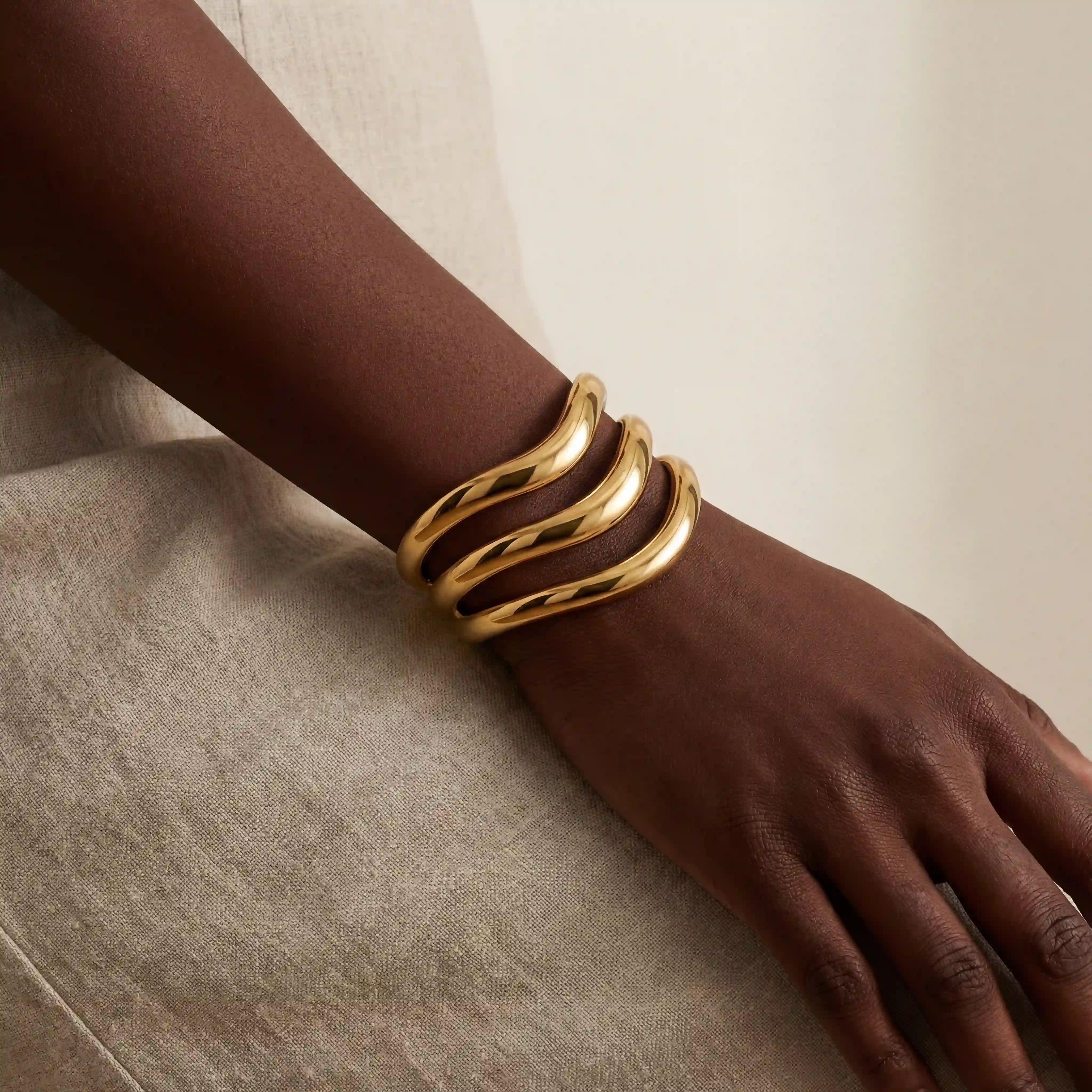 Dark skin model styling sculptural gold instant stack cuff bracelet on wrist. Main image