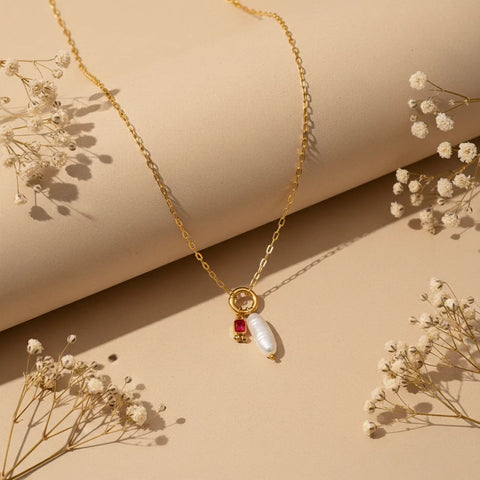 A full view of the personalized Astoria Necklace with the vibrant July birthstone (ruby red), styled with delicate dried flowers.