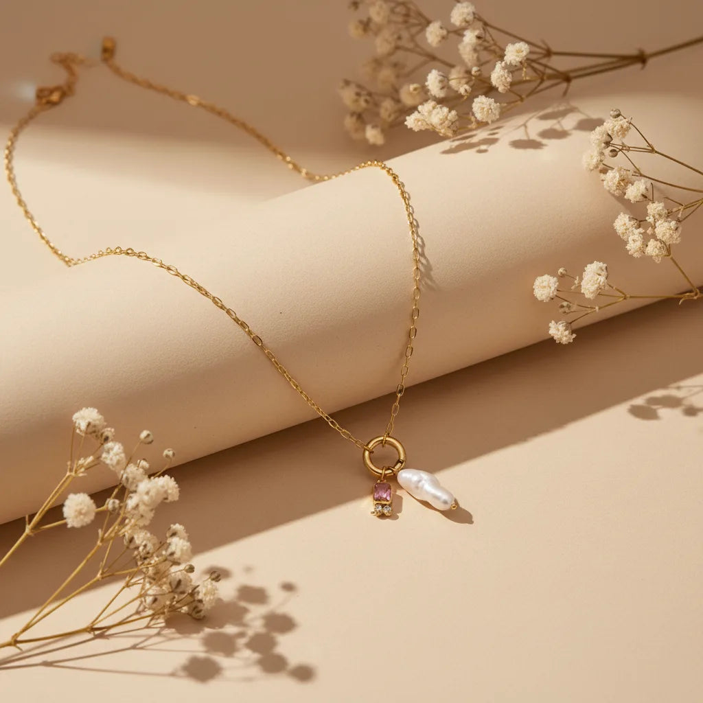 The Astoria Necklace for June, featuring a light purple Alexandrite birthstone and a unique baroque pearl. This personalized gold necklace is styled beautifully with dried baby's breath on a soft, warm background.