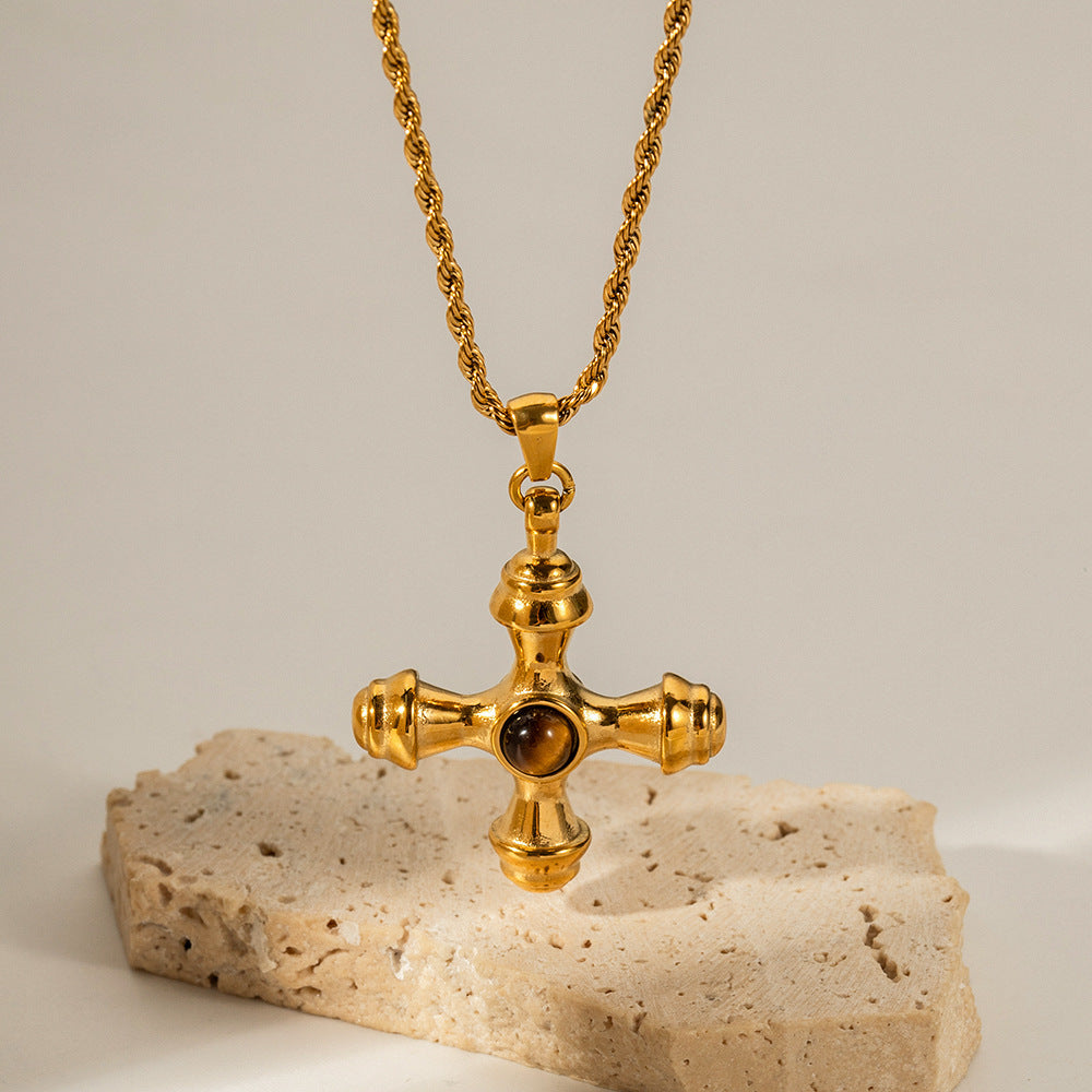 An artistic shot of The Jupiter Necklace with the Tiger Eye cross pendant, styled on a natural, rough stone to emphasize its earthy, powerful aesthetic.