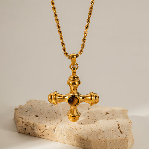 An artistic shot of The Jupiter Necklace with the Tiger Eye cross pendant, styled on a natural, rough stone to emphasize its earthy, powerful aesthetic.