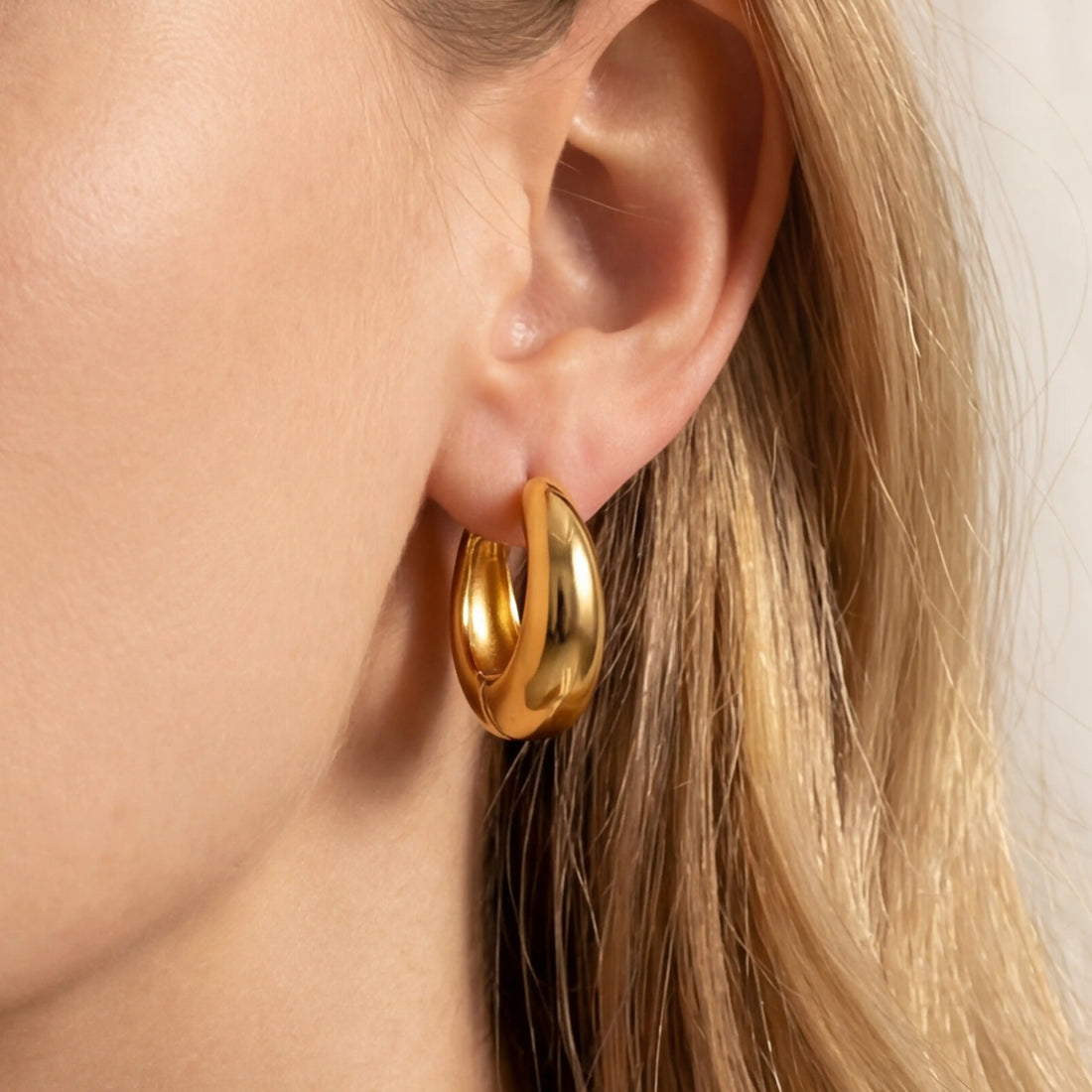 Gold teardrop hoop earrings on ear, lightweight chunky gold hoops for women, hypoallergenic stainless steel waterproof jewelry.