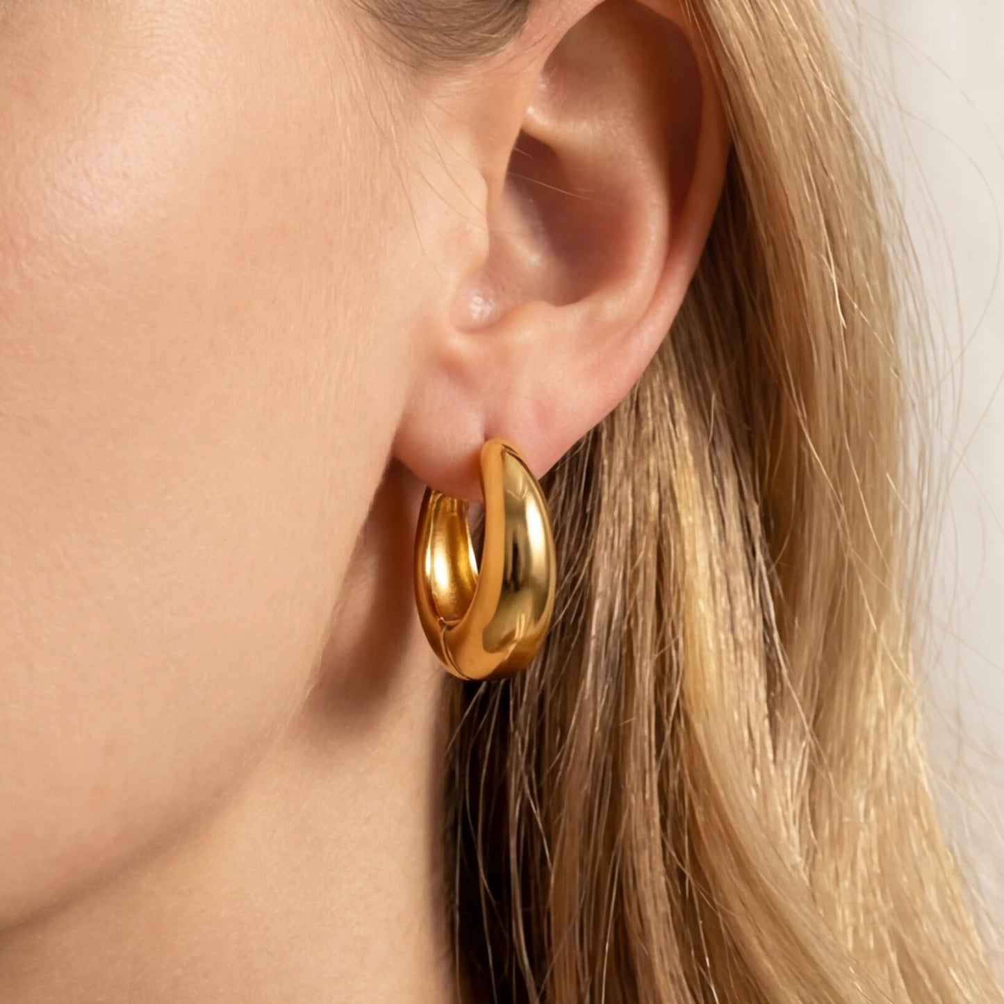 Gold teardrop hoop earrings on ear, lightweight chunky gold hoops for women, hypoallergenic stainless steel waterproof jewelry.