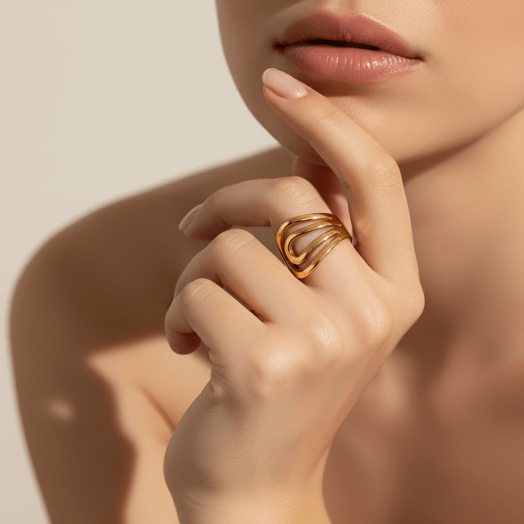 A close-up of a model's hand, showcasing the wide, sculptural Liquid Gold Ring worn on her index finger. Her fingers are slightly curled to highlight the ring's fluid, abstract lines and high-polish finish.