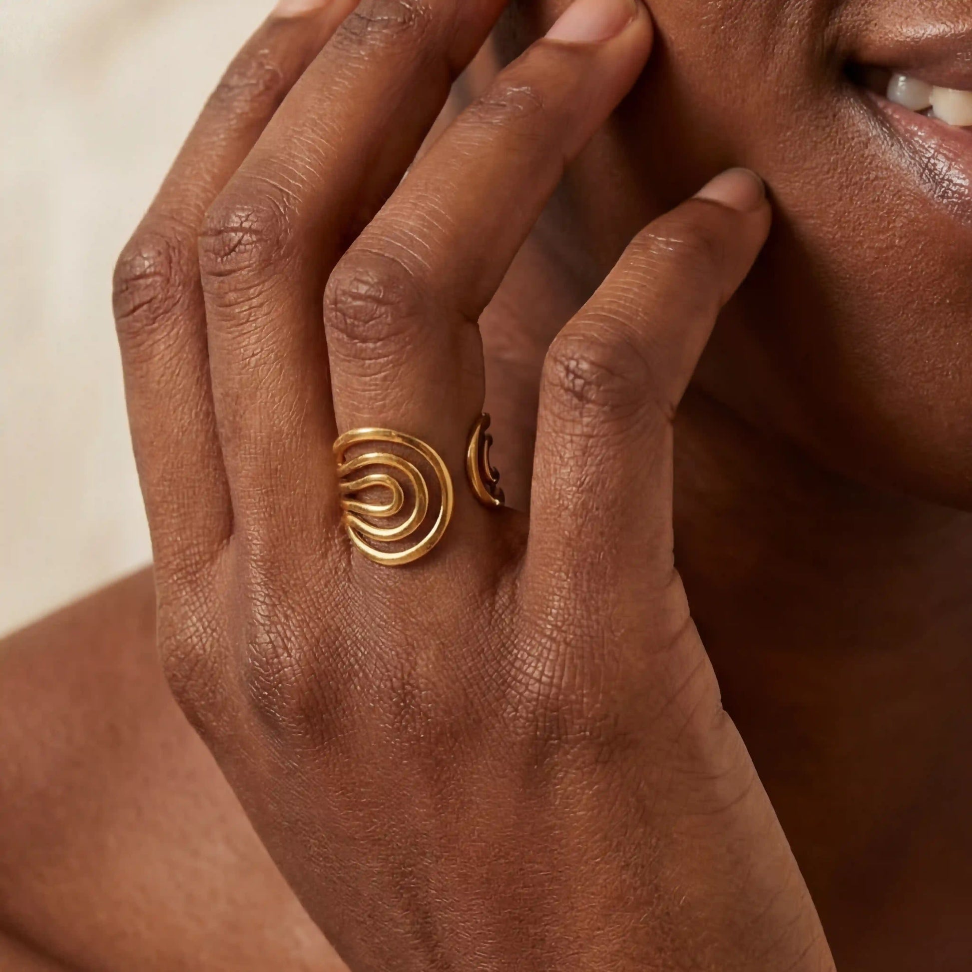 Close up of woman with dark skin wearing liquid gold wave ring statement jewelry.