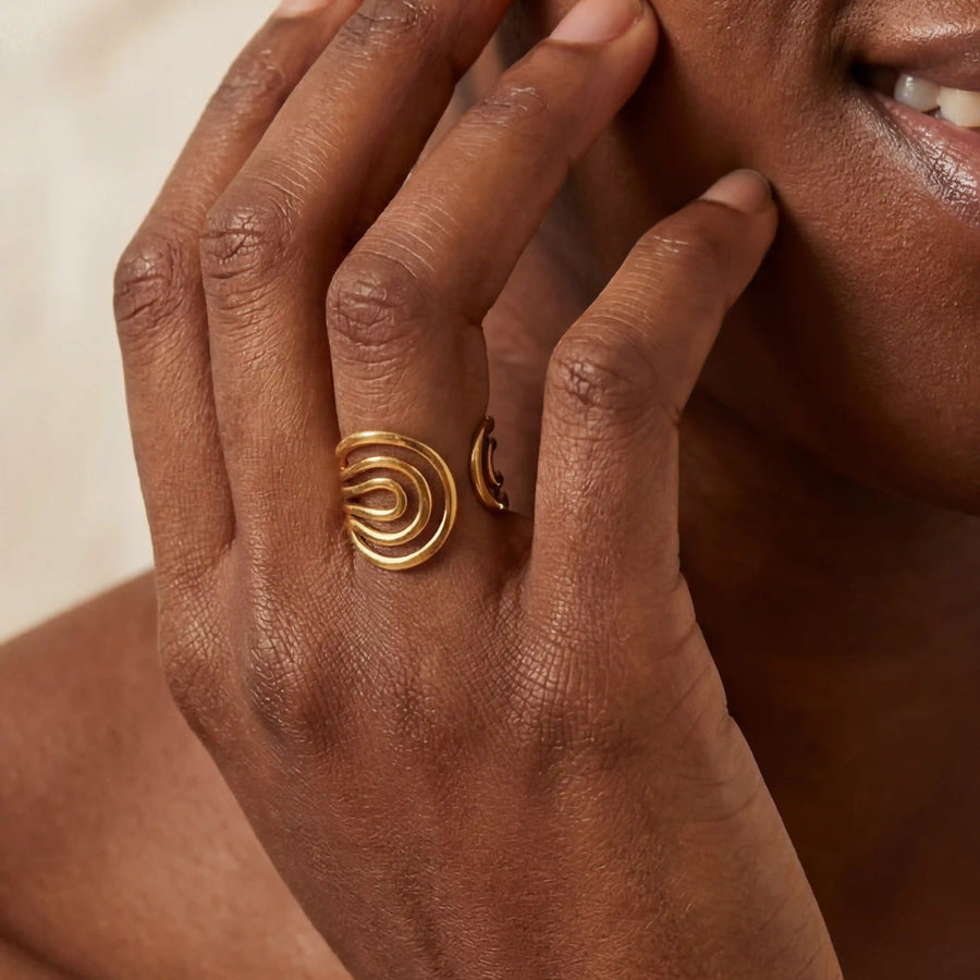 Close up of woman with dark skin wearing liquid gold wave ring statement jewelry.