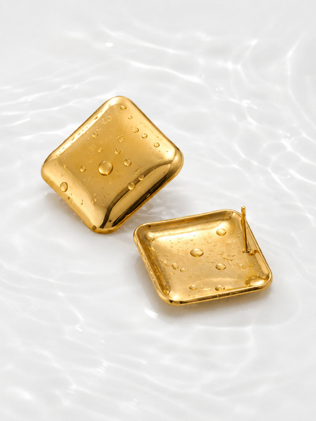 Gold square dome earrings with water droplets on white water ripple background
