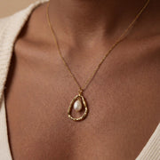 Close up of woman wearing gold Luna necklace with organic open circle and baroque pearl pendant.