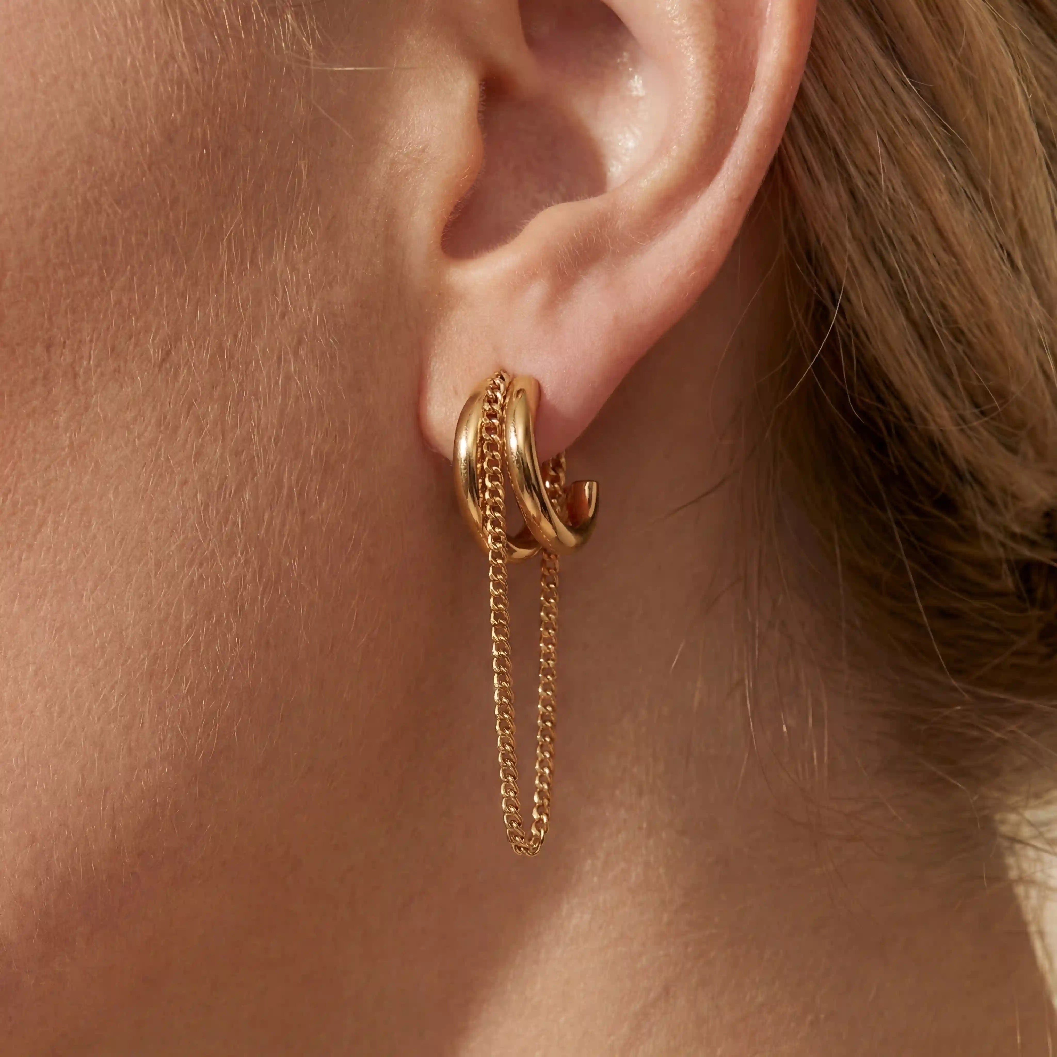 Close up of woman wearing gold luxe layered chain hoop earrings with dangling chain detail. Main image