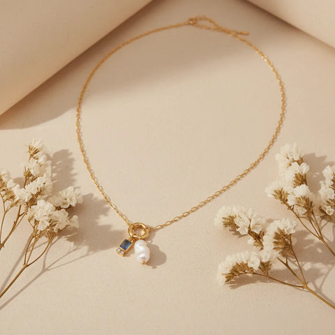 The Astoria Necklace with the serene March birthstone (aquamarine blue), displayed in warm sunlight, perfect as a meaningful birthday gift.