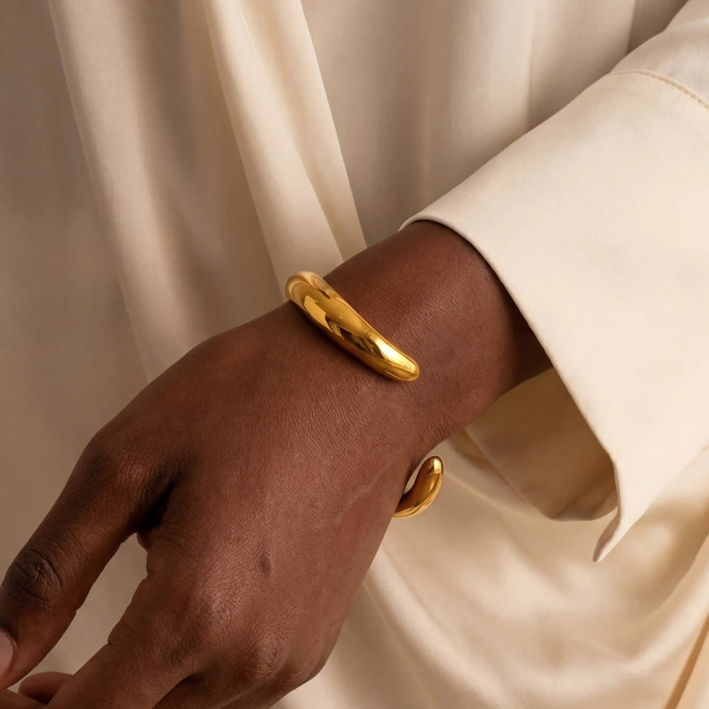 Close up of woman with dark skin wearing gold minimal wave open bangle sculptural design.