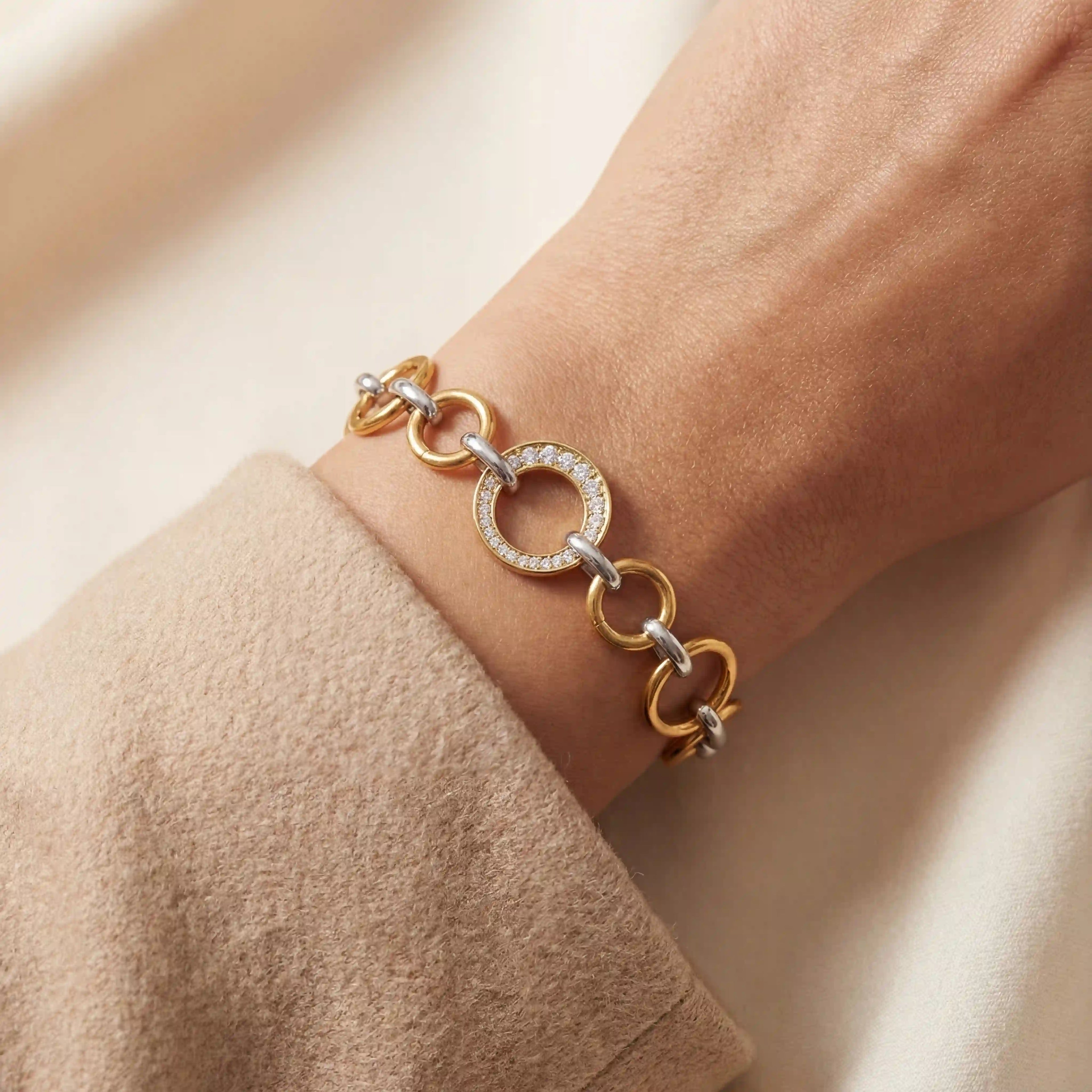 Close up of woman wearing mixed metal interlocking bracelet with gold and silver links and crystal detail.