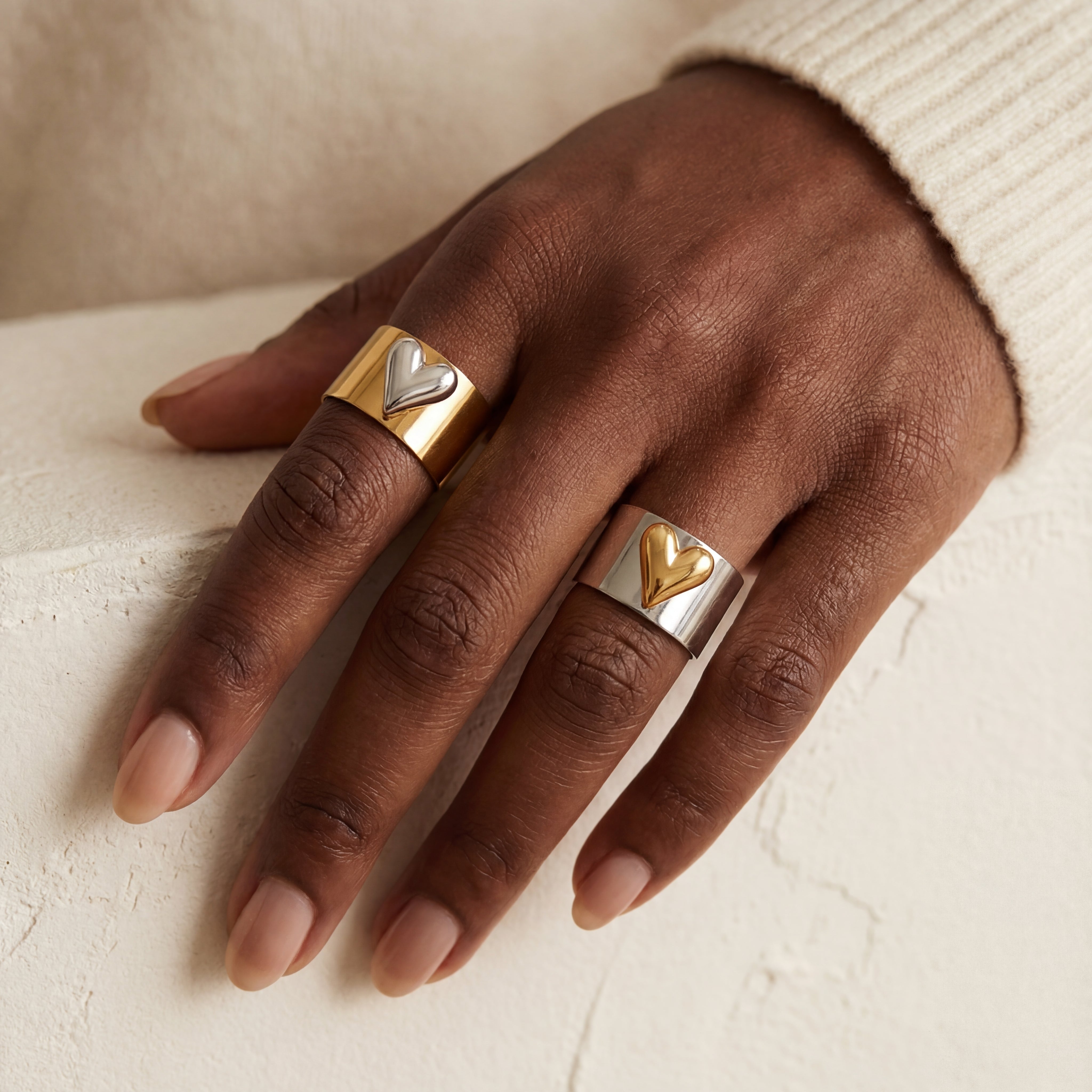 Close up of dark skin woman styling two mixed metal heart rings gold and silver wide bands on one hand.