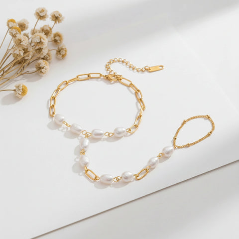 A detailed studio shot of The Nereid Hand Chain by Luminova, showing the delicate bracelet-ring design with freshwater pearls and gold paperclip links.