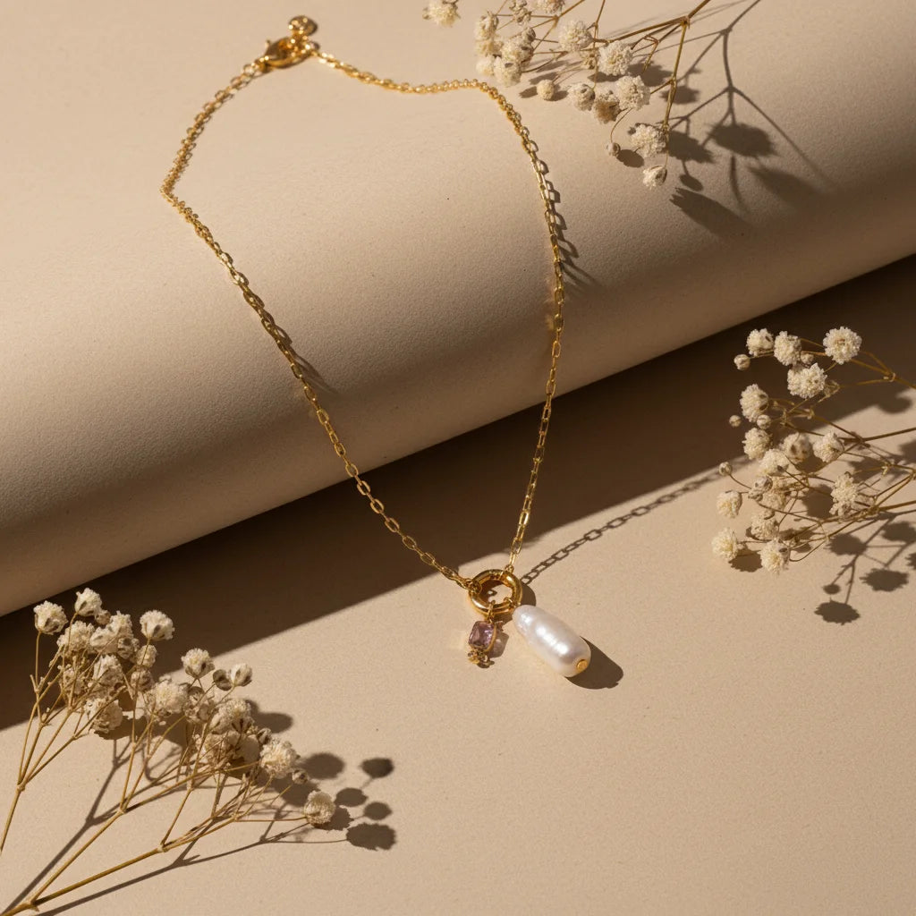 The Astoria Necklace for October, featuring a beautiful pink tourmaline birthstone charm paired with a unique baroque pearl on a gold chain.