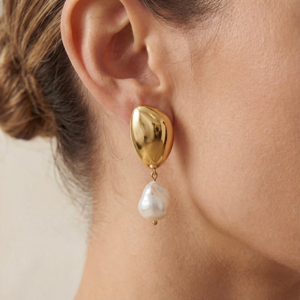 Close up of organic gold teardrop stud earring with baroque pearl drop on woman ear.