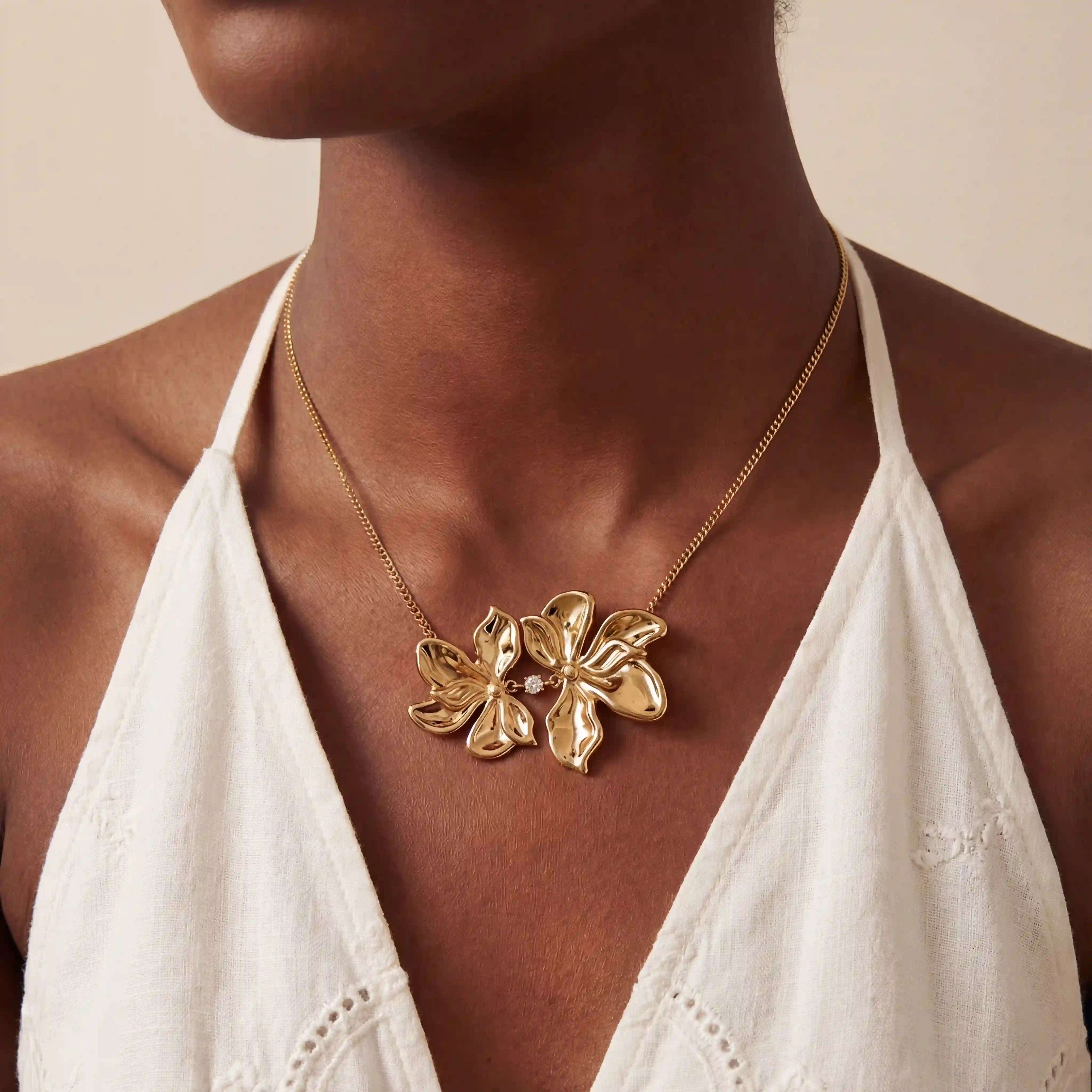 Close up of woman wearing gold Persephone necklace with large sculptural double flower pendant. Main image