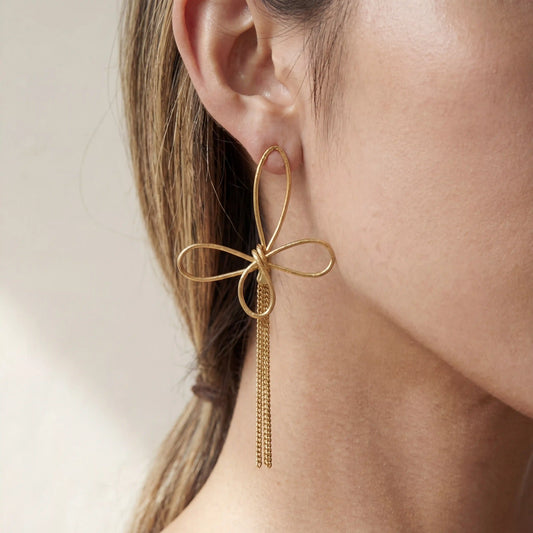 Close up of woman wearing gold Psyche earrings with abstract wire butterfly design and long chain tassels.