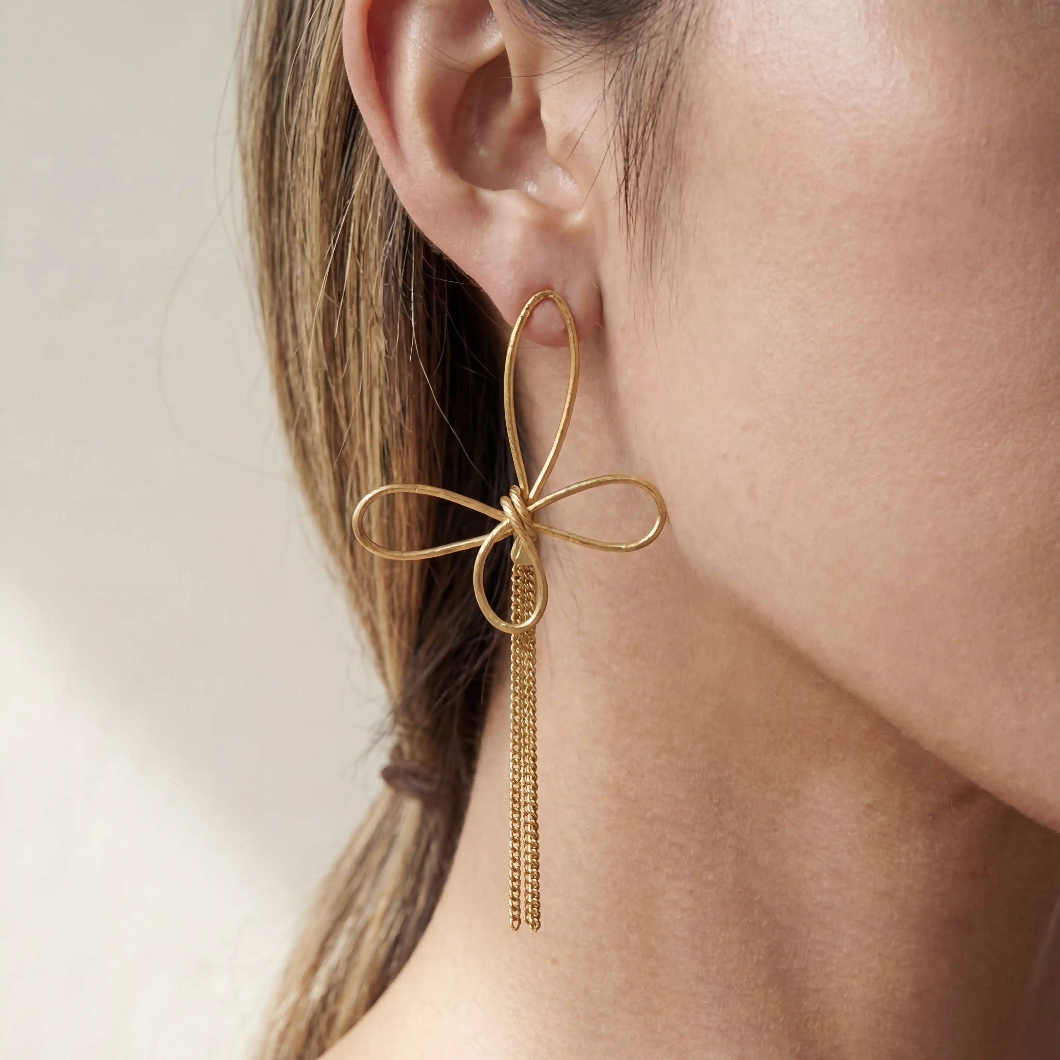 Close up of woman wearing gold Psyche earrings with abstract wire butterfly design and long chain tassels. Main image
